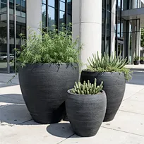 Tall monolithic slate-hued planters arranged on a crushed stone surface. Bespoke exterior styling elements tailored for modernist residences and high-end spec builds.